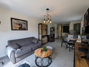 A modern living room with a grey sofa, a wooden coffee table, and a kitchen in the background.