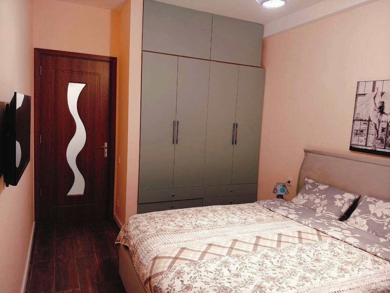 Un dormitorio con cama, armario, una puerta de diseño único y un cuadro colgado en la pared.