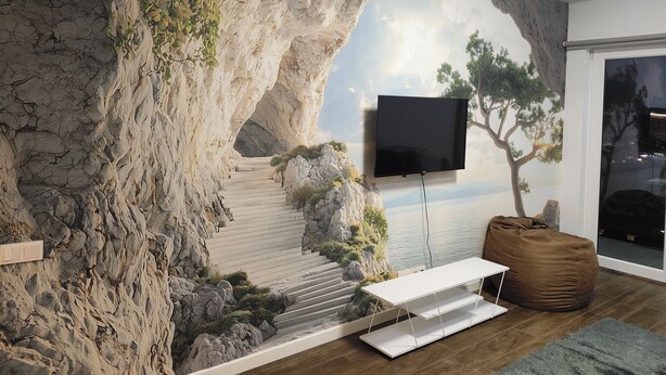 Una sala de estar con un gran mural de un paisaje rocoso, un televisor de pantalla plana montado en la pared, una mesa blanca y un sillón de cuero color café.