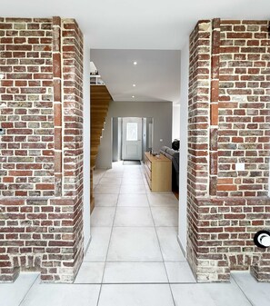 Un couloir aux murs en briques, au sol carrelé, et un escalier menant à un palier.