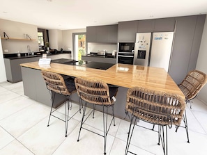 A modern kitchen with a central island, bar stools, and a refrigerator with magnets. - Charming 4-Star Rectory - Somme Bay (Huchenneville)