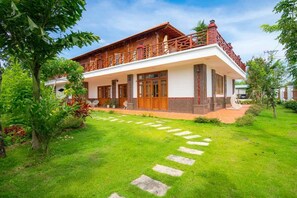 Uma casa de dois andares com varanda, um jardim com pedras no caminho e céu claro.