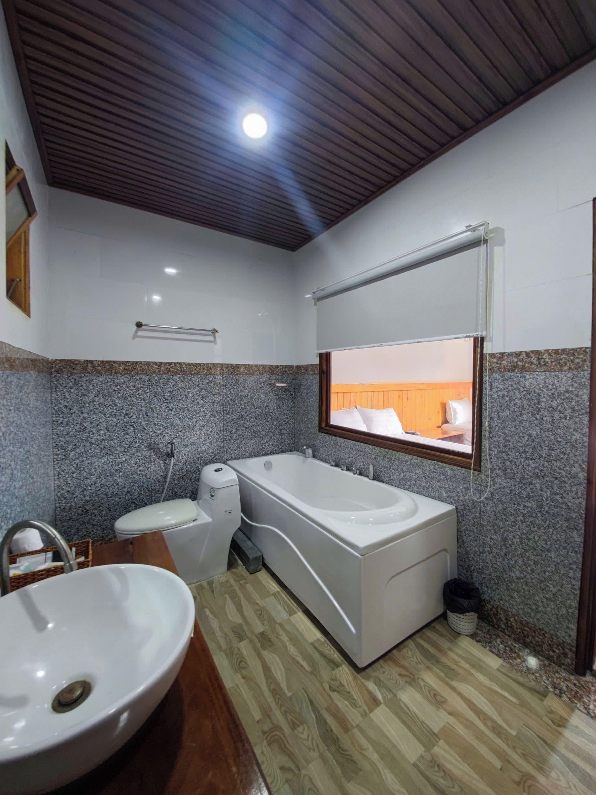 Ein Badezimmer mit Badewanne, Toilette, Waschbecken und einem Fenster mit Blick nach außen.
