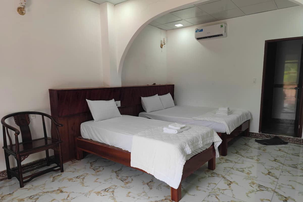Habitación de hotel con dos camas, una silla de madera y suelo de baldosas.