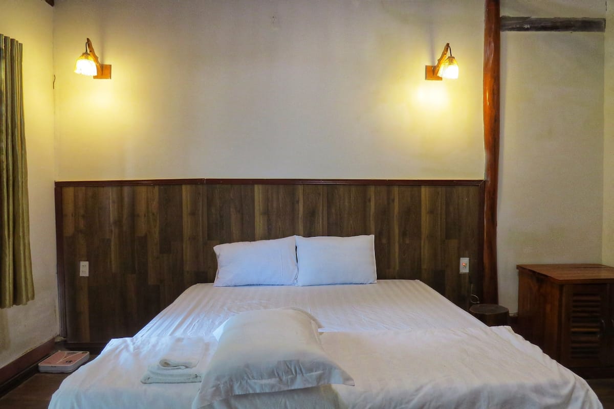 Una cama bien hecha con sábanas y almohadas blancas, un cabecero de madera y dos lámparas fijadas a la pared.