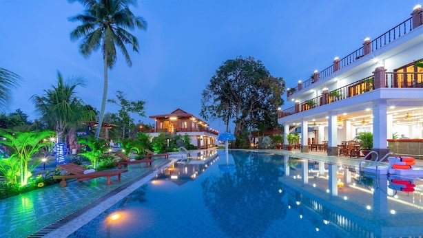A swimming pool with lounge chairs, a building with multiple balconies, and a palm tree. - Serene Resort in Bai Vong Phu Quoc (Phu Quoc)