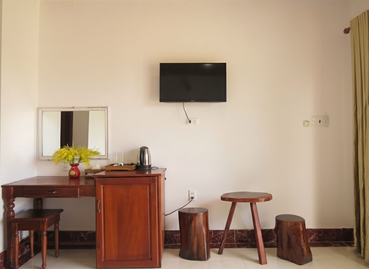 A room with a wooden desk, a mirror, a television mounted on the wall, and two wooden stools.