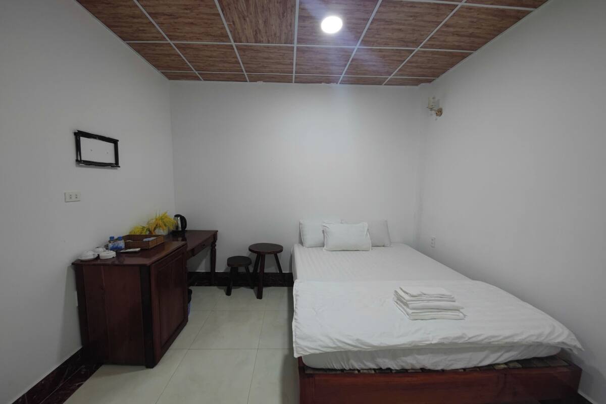 Un dormitorio con techo de madera, una cama con ropa blanca, un escritorio con una silla y un taburete pequeño.
