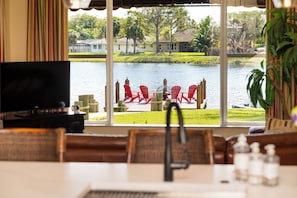 A dining area with a view of a lake, red chairs, a television, and a plant. - Waterfront 3BR! Spacious Dock, King Bed, BBQ (Delray Beach)