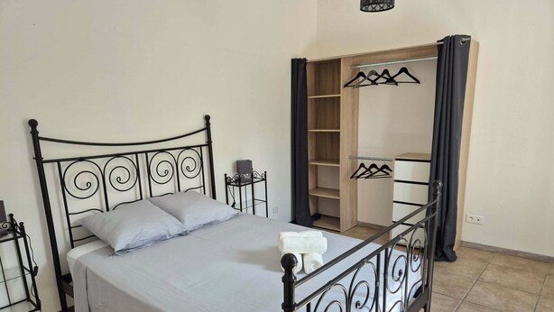 Una cama con estructura metálica, una mesita de noche, un armario con espejo y una percha para ropa.