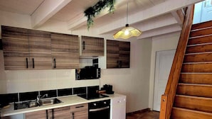 Una cocina con armarios de madera, encimera blanca, un lavabo, estufa, lavavajillas y una escalera de madera.