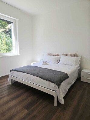 Een slaapkamer met een bed, een nachtkastje, een raam en uitzicht op groen.