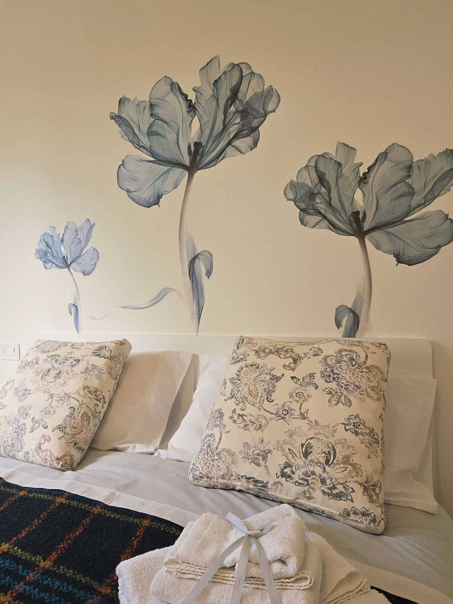 A bed with floral-patterned pillows, a neatly folded towel, and a wall with a floral mural.