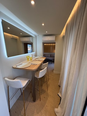 A modern dining area with a wooden table, white chairs, and an air conditioning unit on the wall. - Terrace 20 m2 Top Floor - 2-room apartment (Nice)