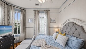 Ein Schlafzimmer mit einem Bett, einem Fernseher, einem Nachttisch und einem Fenster mit Vorhängen.