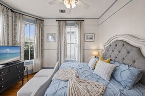Quarto com cama, televisão, mesa de cabeceira e janela com cortinas.