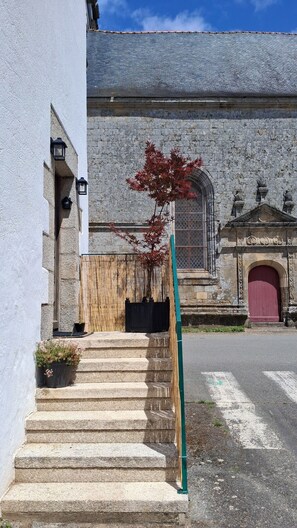 A stone staircase leading to a building with a red door, a small tree, and a wooden fence.