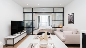 Een moderne hotelkamer met een flatscreen televisie, een zithoek met een tafel gedekt voor twee personen, een bank en een groot raam met gordijnen.
