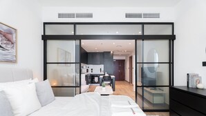 Een moderne slaapkamer met een groot bed, een glazen scheiding, een keukenhoek en uitzicht op de woonruimte.