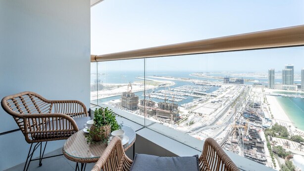 Een balkon met rieten meubels, een tafeltje en een bloempot.