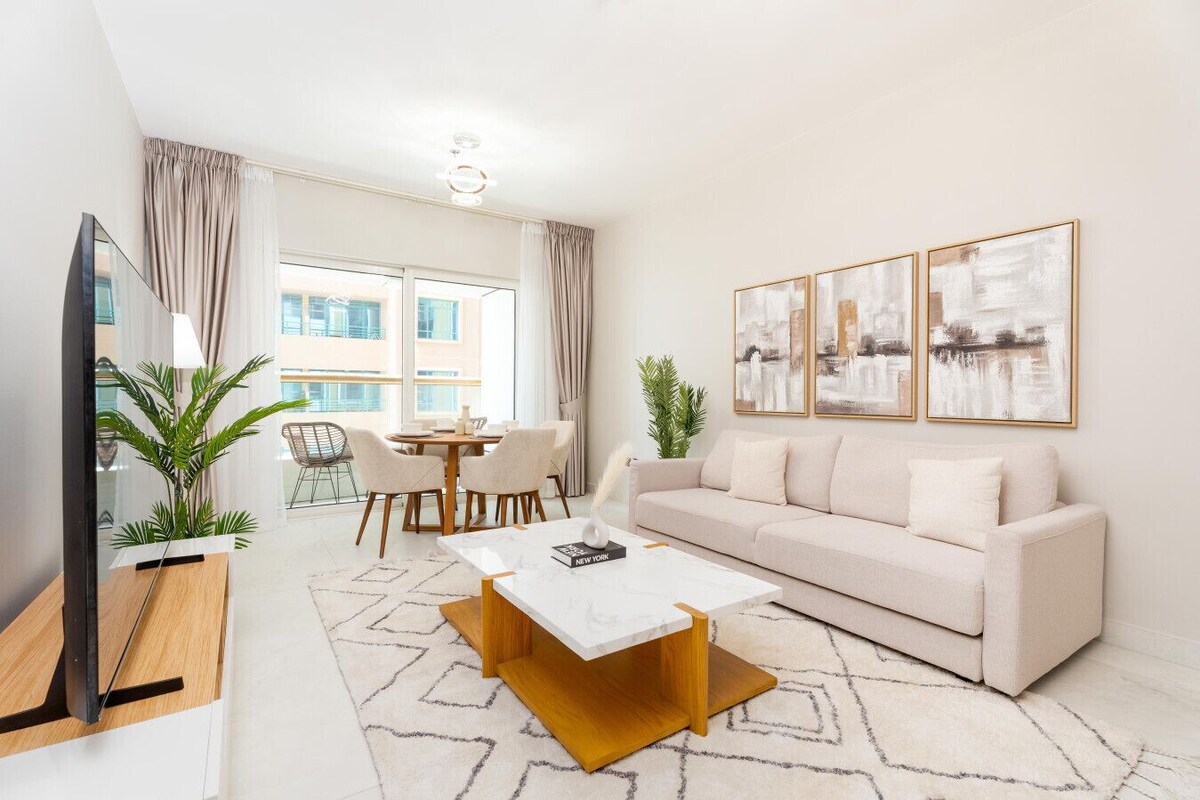 En moderne stue med sofa, sofabord, fjernsyn, spiseområde og kunstværker.