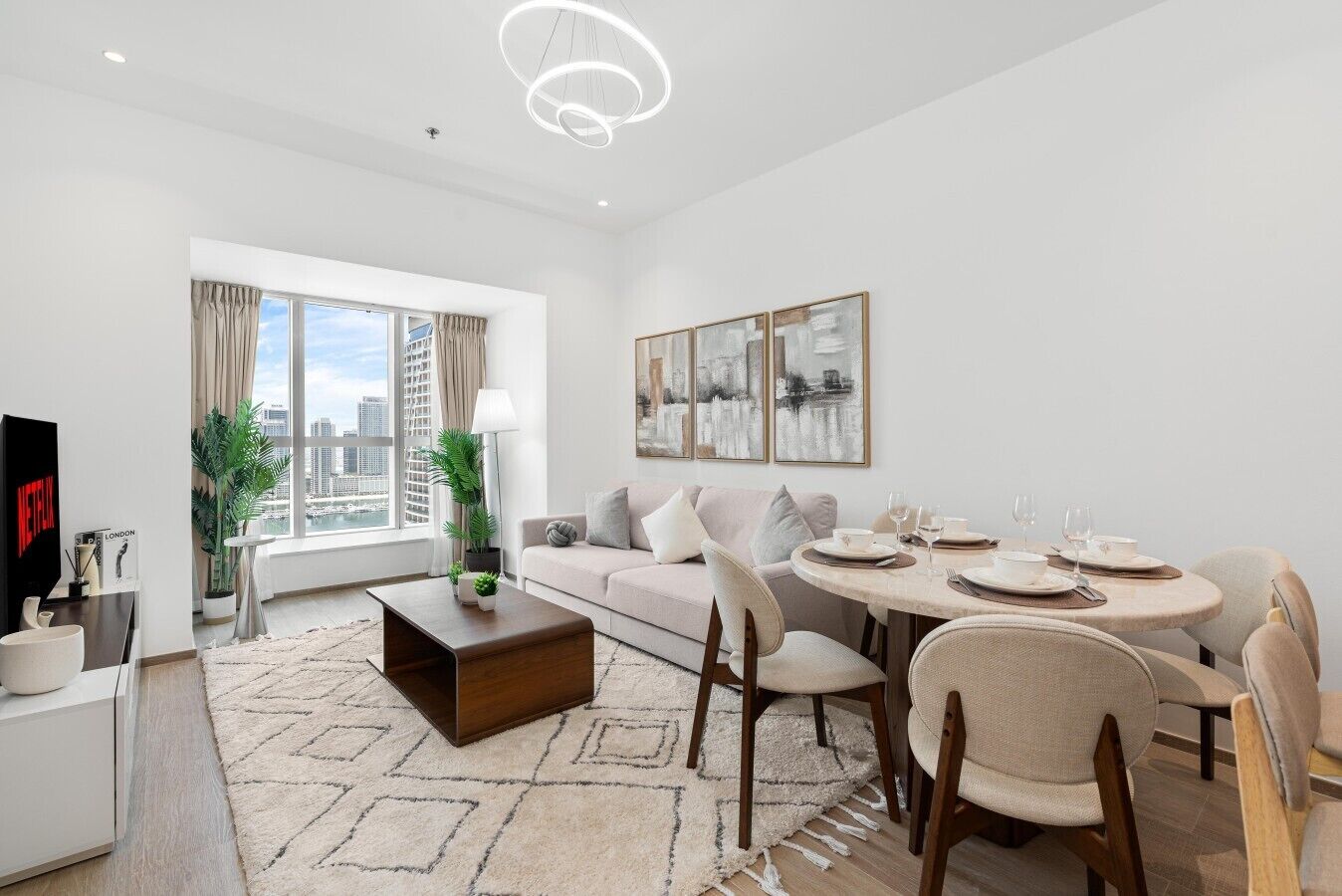 A modern living room with a sofa, coffee table, dining table with chairs, a TV, and artwork on the wall.