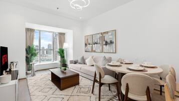 A modern living room with a sofa, coffee table, dining table with chairs, a TV, and artwork on the wall.