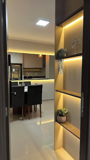 A modern kitchen with built-in appliances, a dining area with a table and chairs, and a decorative shelf with plants.