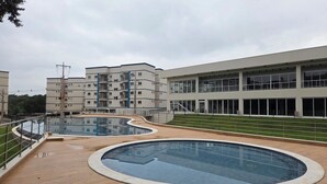 A modern building with two swimming pools, a grassy area, and a multi-story structure with balconies. - 3-bedroom condo with beautiful views, pool, gym & gardens at Salto del Monday (Franco)
