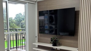 A modern living room with a flat-screen TV, a sofa, a coffee table, and a balcony with a railing. - 3-bedroom condo with beautiful views, pool, gym & gardens at Salto del Monday (Franco)