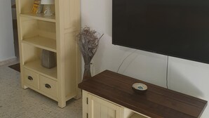 A living room with a TV, wooden entertainment unit, and a painting on the wall. - Latchi Harbour 2-bedroom Penthouse (Poli Chrysochous)