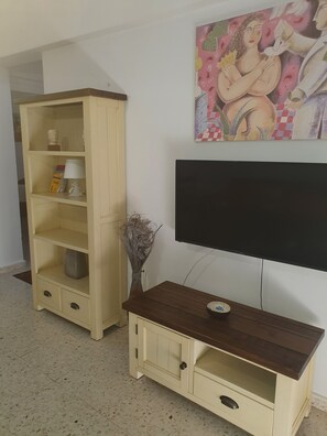Un salon avec un téléviseur, un meuble de rangement en bois et un tableau accroché au mur.