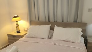 A neatly made bed with white linens and rolled towels, a bedside lamp, and a wooden headboard. - Latchi Harbour 2-bedroom Penthouse (Poli Chrysochous)