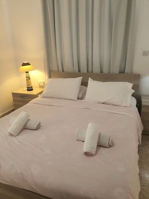 Un lit bien fait, avec du linge de lit blanc et des serviettes pliées, une lampe de chevet et une tête de lit en bois.