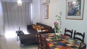A dining area with a checkered tablecloth, wooden chairs, a sofa, and a vase with flowers. - Latchi Harbour 2-bedroom Penthouse (Poli Chrysochous)
