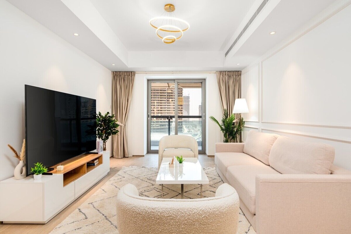 Ein modernes Wohnzimmer mit Flachbildfernseher, einer Couch, einem Couchtisch und Blick auf die Stadt durch ein großes Fenster.