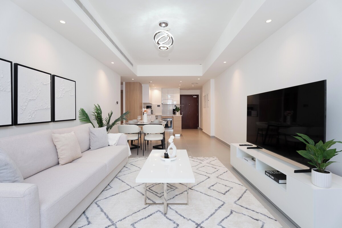 Ein modernes Wohnzimmer mit Sofa, Couchtisch, Fernseher und einer Küche im Hintergrund.