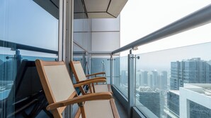 A balcony with three wooden chairs, a glass railing, and a city view. - Gala Guests - Princess Tower Suites (Dubai)