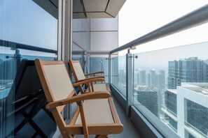 Ein Balkon mit drei Holzstühlen, einer Glastrennwand und Blick auf die Stadt.