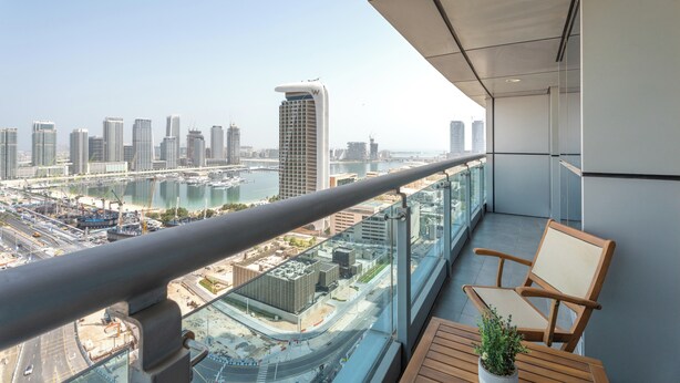 A balcony with a view of a cityscape, a table with a plant, and a chair. - Gala Guests - Princess Tower Suites (Dubai)