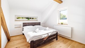 A bedroom with a wooden bed, white bedding, a window with a view, and a small plant on the windowsill.