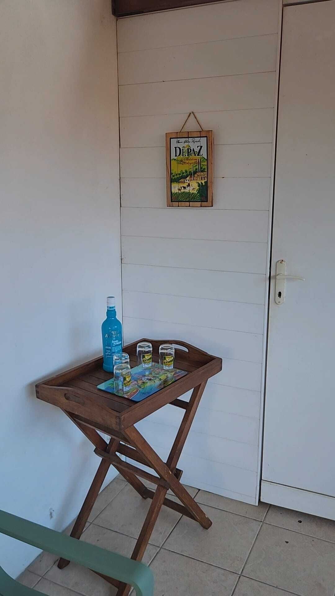 Una pequeña mesa de madera con una botella de agua y dos vasos, un cartel enmarcado en la pared, y una puerta a la derecha.