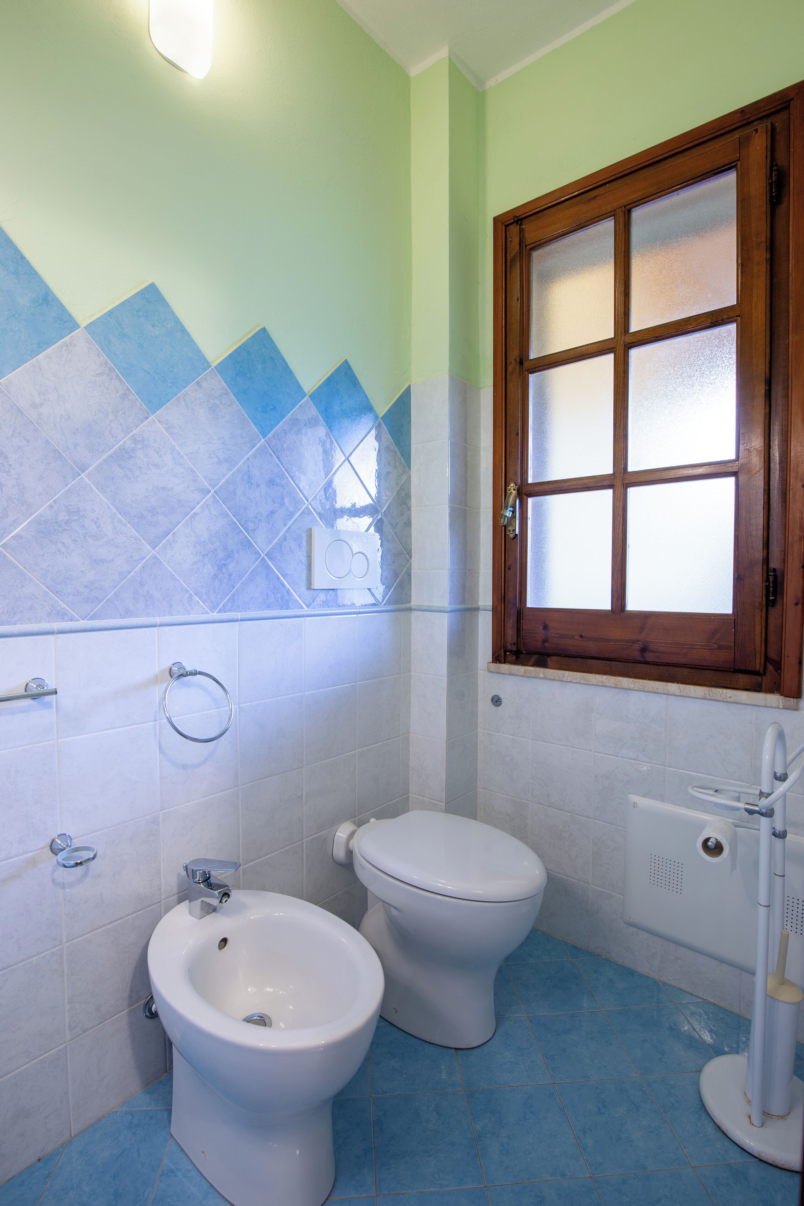 Een badkamer met twee toiletten, een douchetoilet en een raam met gezandstraald glas.