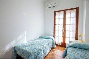 Ein Zimmer mit zwei Betten, einer Klimaanlage, einer Holztür und einem kleinen Schreibtisch mit Lampe.