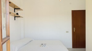 Quarto com cama, prateleiras de madeira, porta e luminária.