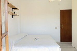 Quarto com cama, prateleiras de madeira, porta e luminária.