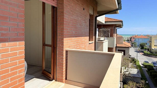 Edifício residencial com fachada de tijolos, porta de correr de vidro e varanda com vista para uma rua e um corpo d'água.