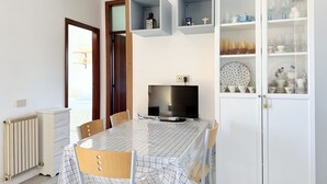 Uma sala de jantar com mesa, cadeiras, televisão e um armário com louças.