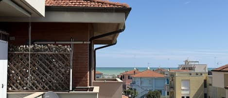 A residential building with a balcony overlooking a beach, a satellite dish, and a lattice fence.
