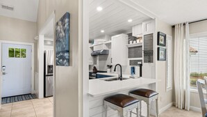 A modern kitchen with a white countertop, two bar stools, a stainless steel refrigerator, and a large window with blinds. - Lakefront Villa with 6 Seat Golf Cart (Miramar Beach)